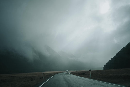 road going through mountains on a misty day with low visibility, car approaching. 