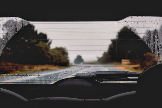 looking out back of car window to road behind, raining grey skies. raindrops on window glass