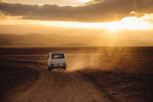 white van driving down a gravel road into the sunset