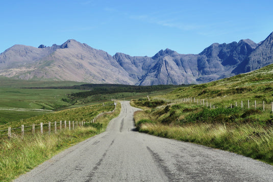 clear blue skies, rugged mountain range in distance, green grass, driving along the gravel road.