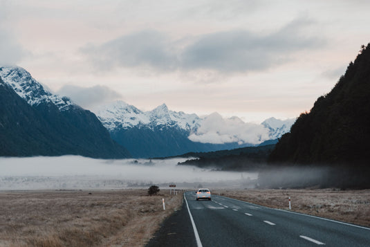 cloudy skies, rugged snowy hills, morning light, misty cloud cover through valley, travelling behind a white car.