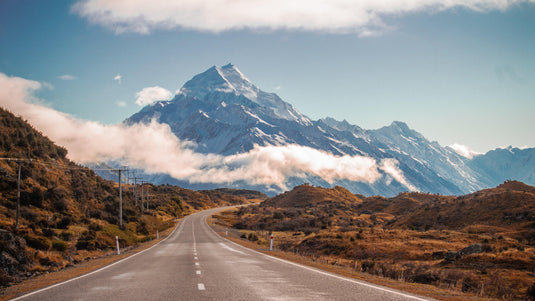 clear blue skies, winters day, mount cook new zealand in the distance, low cloud hovering to the side of a winding road.