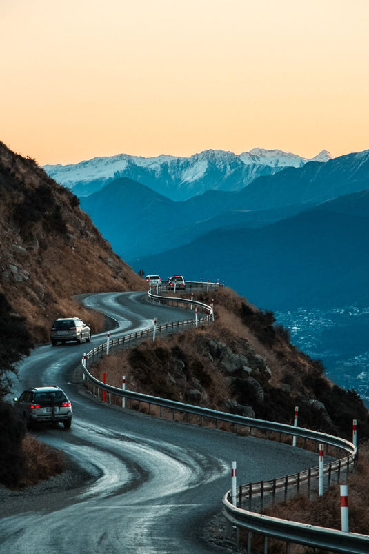 Cars driving through windy NZ road up a hillside at sunset, pink sky